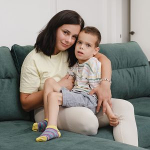 Mother with disabled child on sofa. Woman hugging boy with cerebral palsy at home. Mother having fun, taking care of handicap boy Leisure time together. Child development games at home.