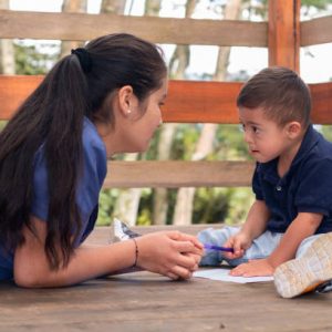 Woman in blue uniform teaching writing to a child with Down syndrome. Children's occupational therapy.